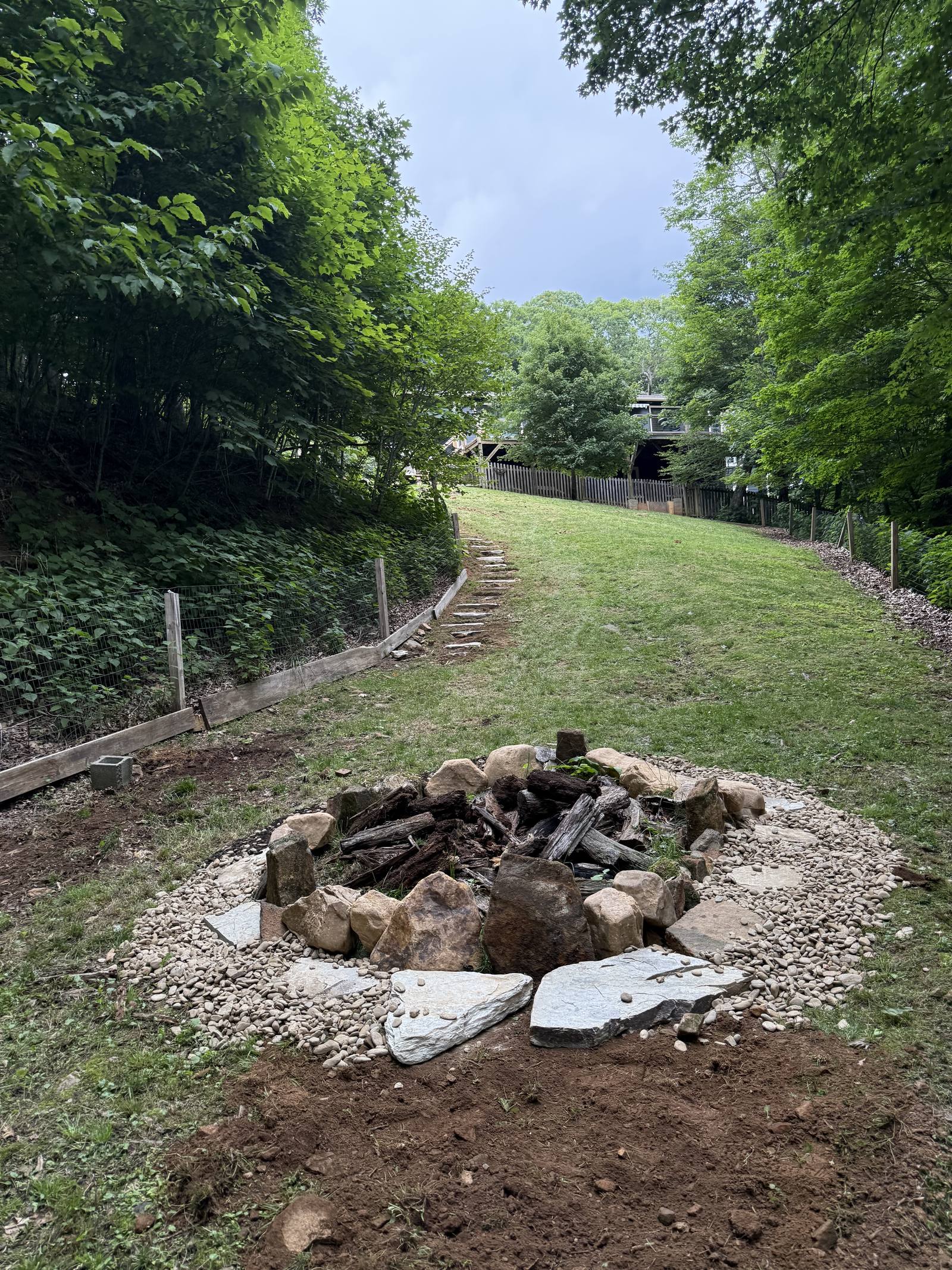 A stone fire pit ringed with river rock at the bottom of a freshly seeded slope